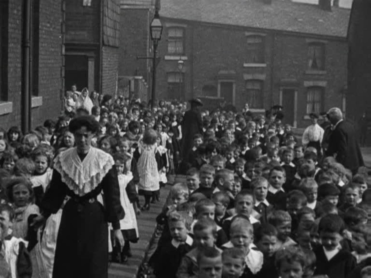 Edwardian primary schoolchildren are marshalled along the streets of Blackburn in strict formation.