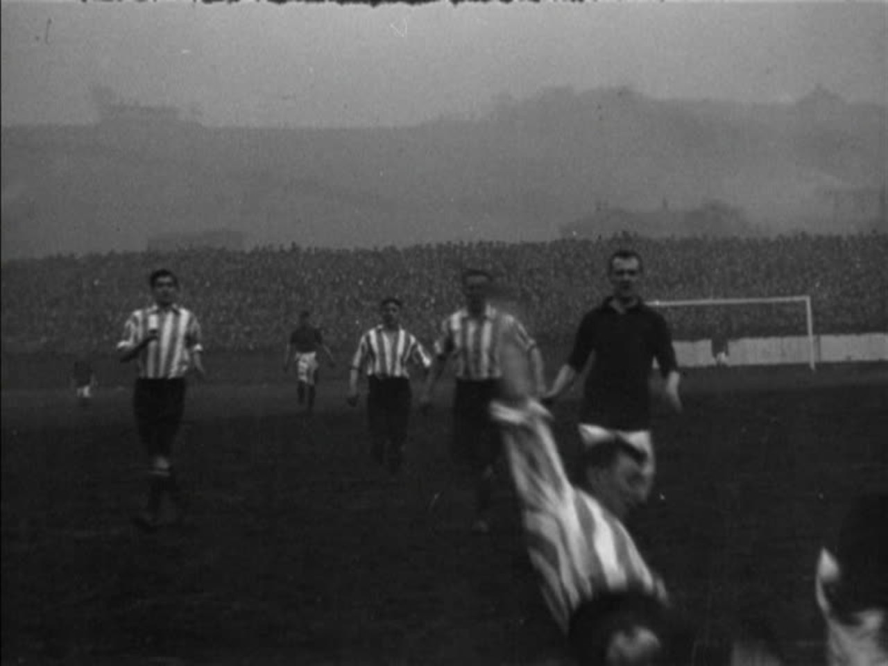 A large and lively crowd watches an Edwardian Second Division football match at Burnley's Turf Moor ground.