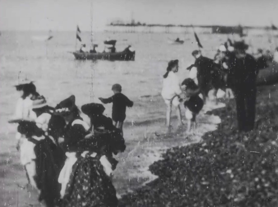 A charming image of children paddling on a pebbly beach on a hot summer's day