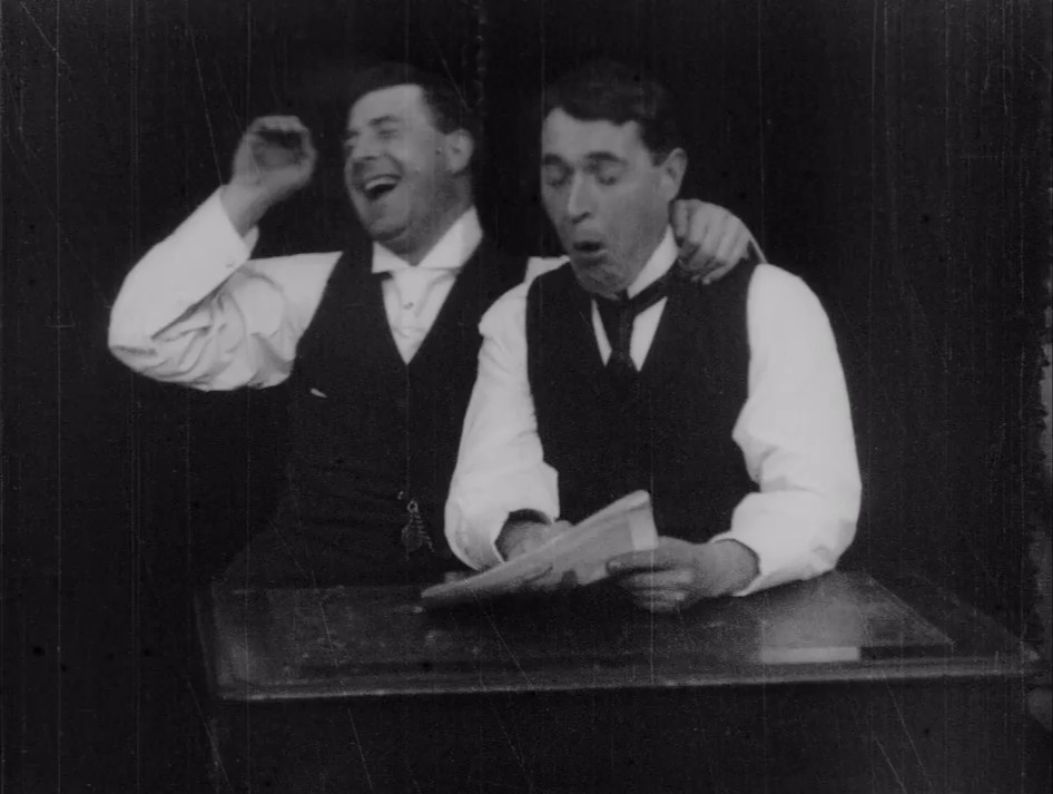Two men lose it laughing at something in a magazine